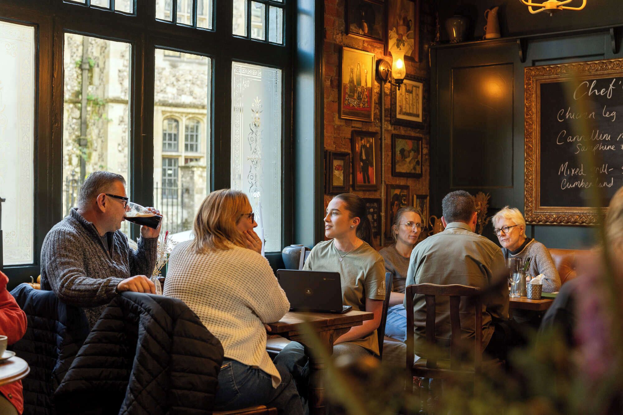 Un café chaleureux où les clients sont assis à des tables, avec de grandes fenêtres et un menu écrit à la craie.