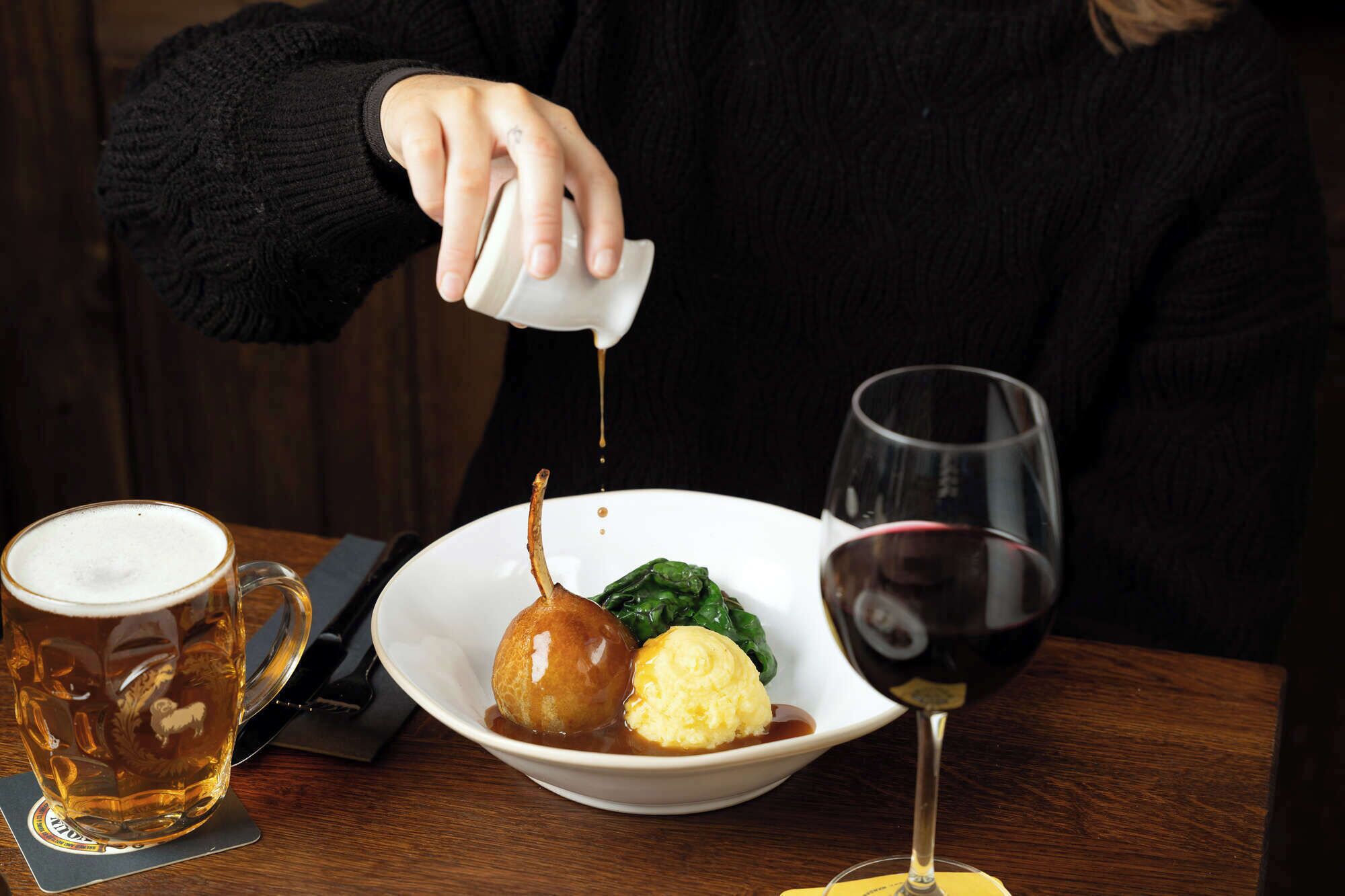 A person pouring a liquid from a small white container onto a plate with food.