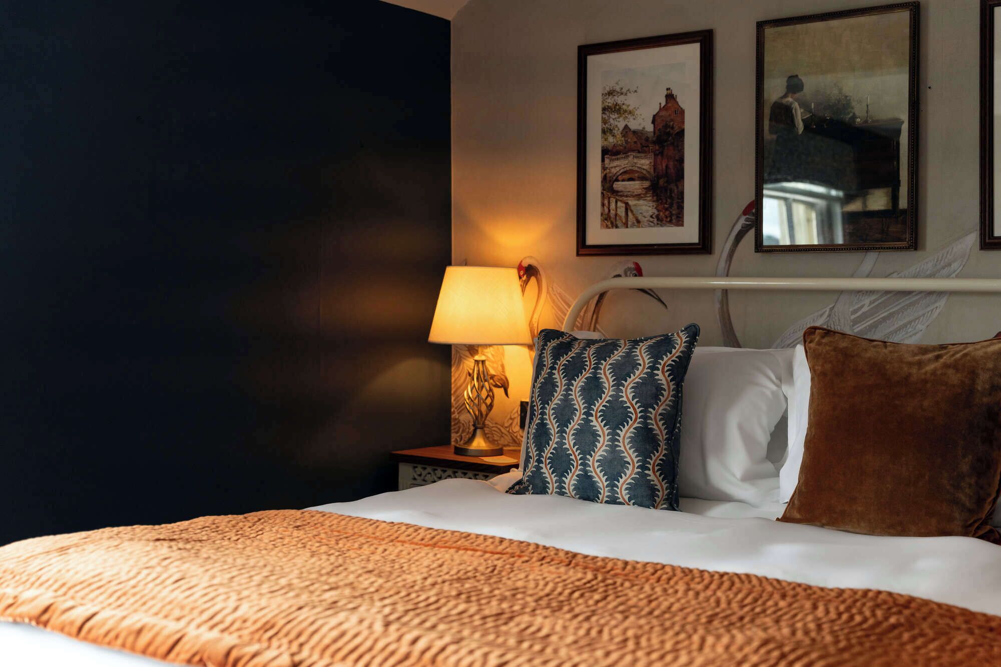 Ein Hotelzimmer mit Bett, Nachttisch mit Lampe und zwei gerahmten Bildern an der Wand.