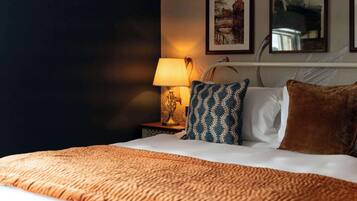 Ein Hotelzimmer mit Bett, Nachttisch mit Lampe und zwei gerahmten Bildern an der Wand.