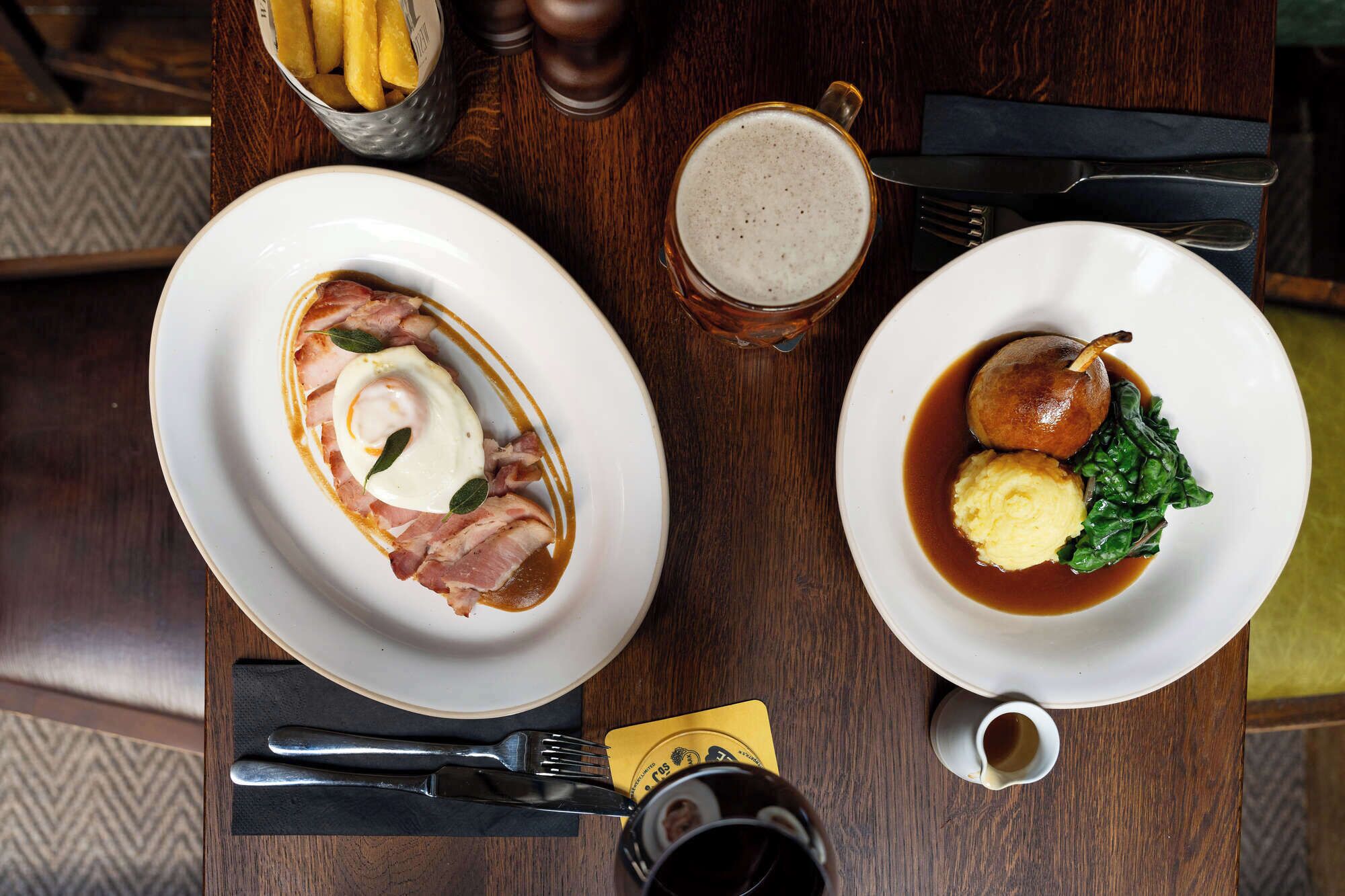 Two plates of food, a glass of beer, and a cup of coffee on a wooden table.