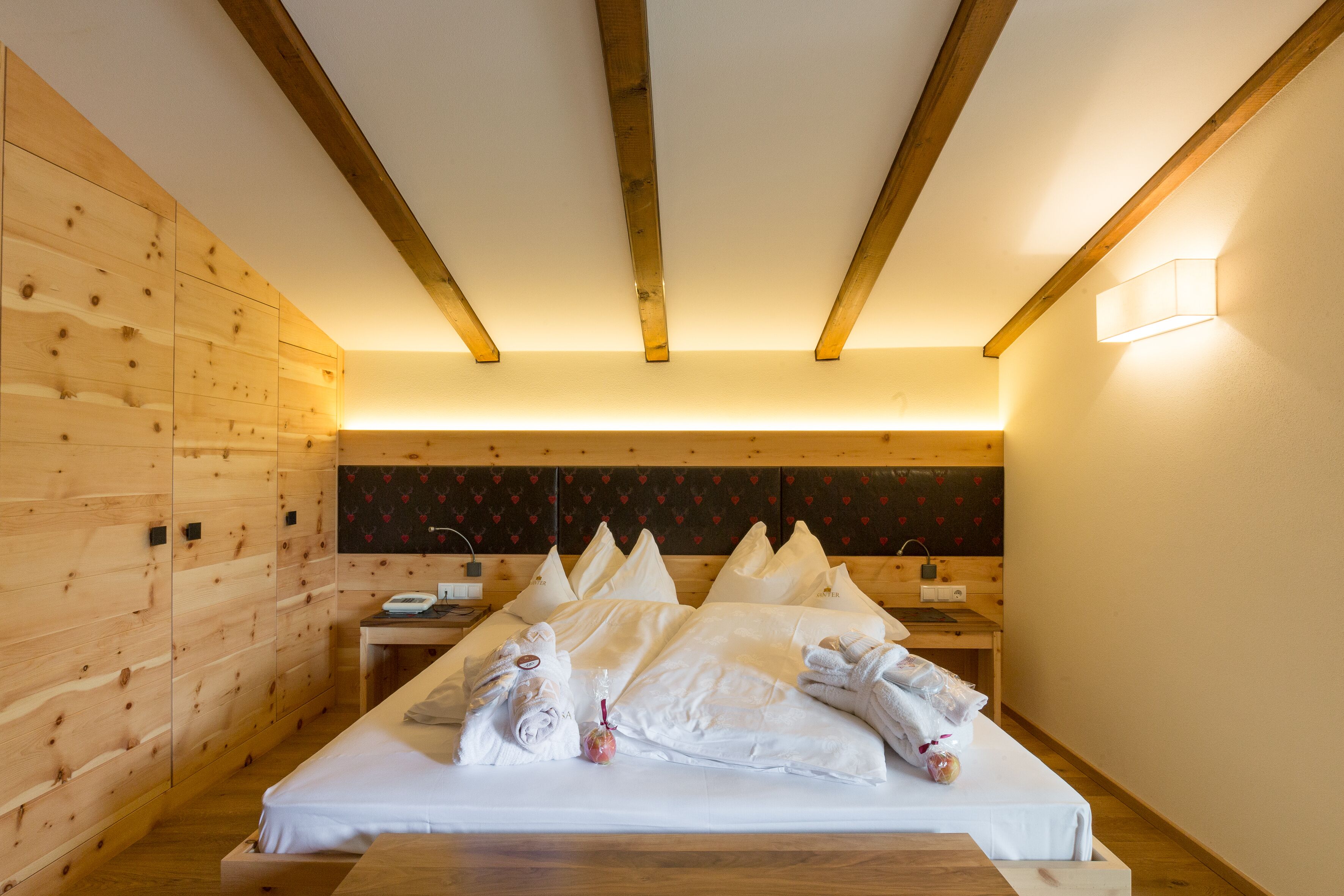 Une chambre d’hôtel avec un mur en bois, un lit avec du linge de lit blanc et une table de chevet avec une lampe.