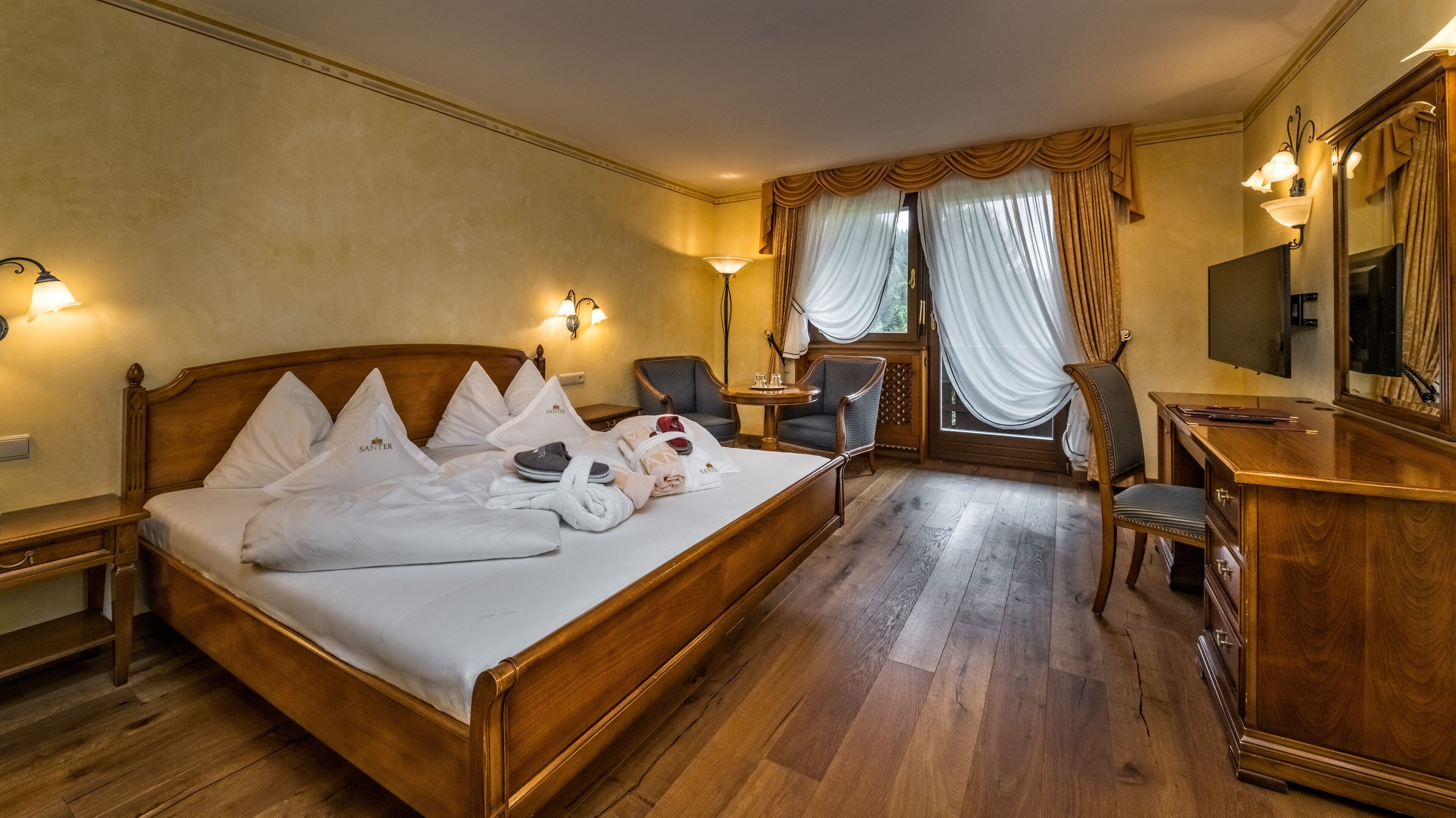 A hotel room with a wooden bed, a desk, a chair, a television, and a window with curtains.
