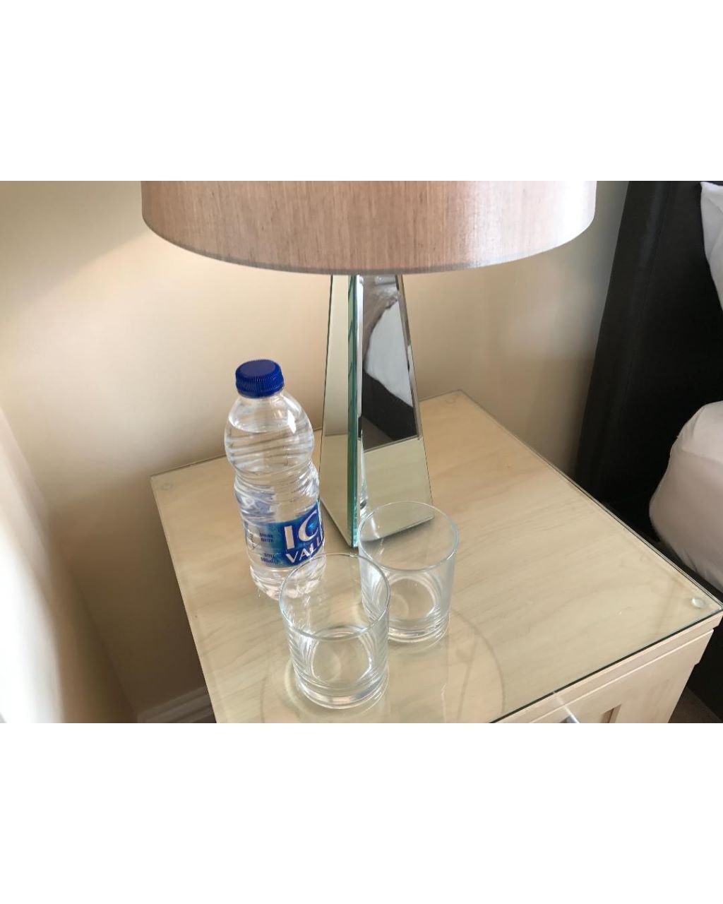 A bedside table with a water bottle, a glass, and a lamp.
