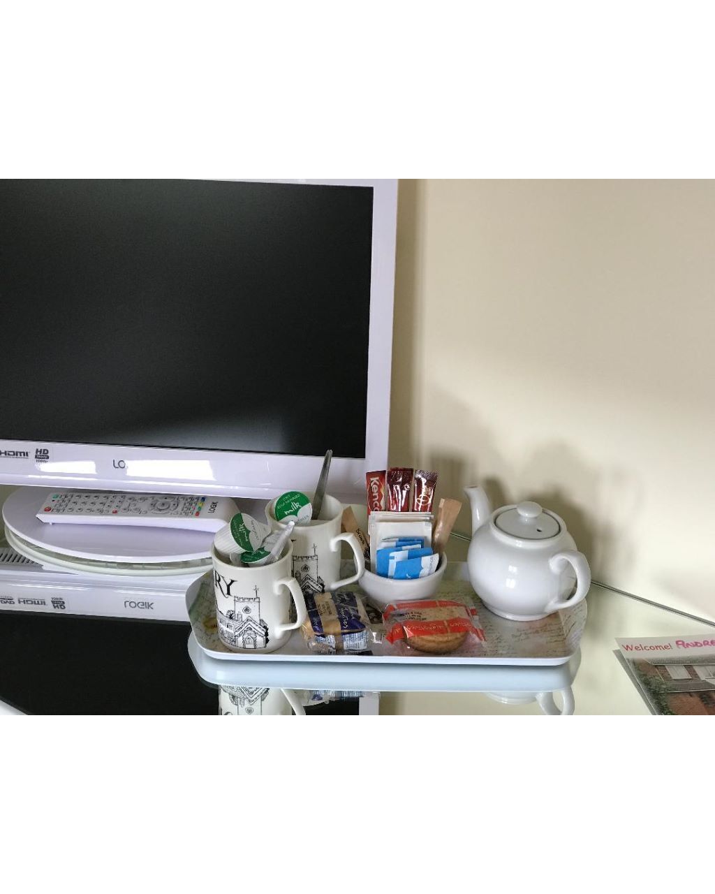 A desk with a computer monitor, a mug, a teapot, and some food items.