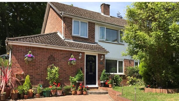 A two-story house with a brick facade, a tiled roof, and a front entrance. There are potted plants and flowers around the entrance, and a brick pathway leading to the door. - 31 Queens Road (Winchester)