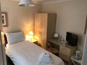 Una habitación de hotel con cama, armario, escritorio con televisor y una silla.