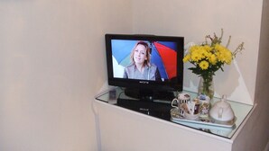 A television on a glass table with a vase of yellow flowers and a mug. - 31 Queens Road (Winchester)