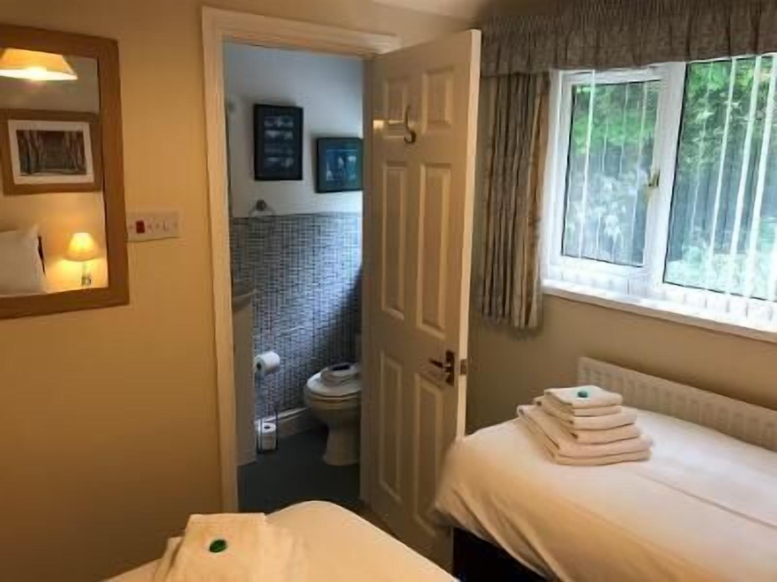 Habitación de hotel con cama, ventana con cortinas, baño visible a través de una puerta abierta y una lámpara fijada a la pared.