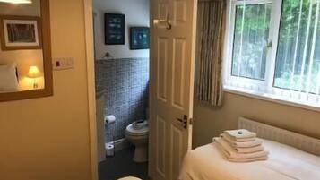 Habitación de hotel con cama, ventana con cortinas, baño visible a través de una puerta abierta y una lámpara fijada a la pared.