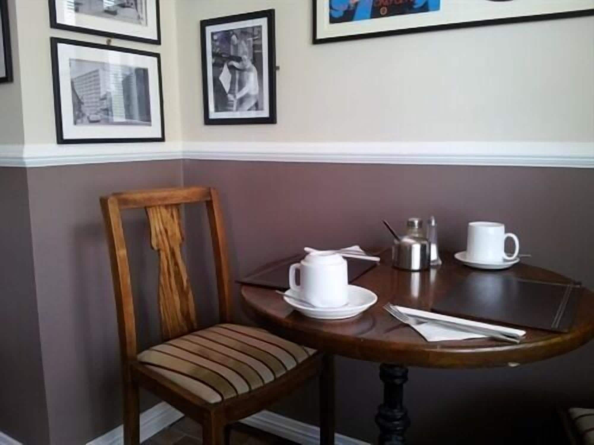 A dining area with a wooden chair and a round table set with white cups, saucers, and a sugar container.