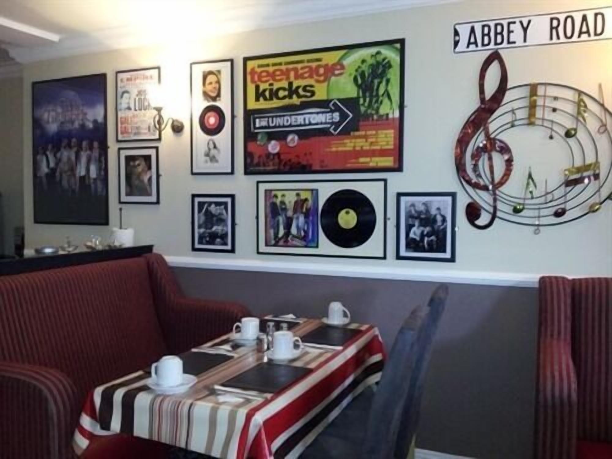 Ein Zimmer mit einer Postern verzierten Wand, einem Schild mit der Aufschrift 'Abbey Road' und einem Tisch, der mit Tassen und Untertassen gedeckt ist.