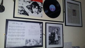 A wall with framed items including a vinyl record, a newspaper clipping, a sheet music, and a black and white photograph. - Abbey Bed and Breakfast (Londonderry)