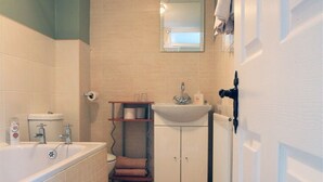 A compact bathroom with a bathtub, toilet, sink, and a small shelf with toiletries. - Abbey Bed and Breakfast (Londonderry)