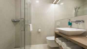 A modern bathroom with a glass shower enclosure, a white sink with a wooden shelf, and a toilet.