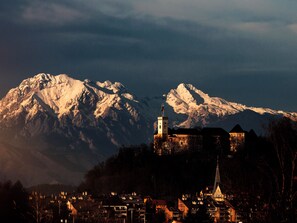 A historic town with a prominent church and castle, surrounded by snow-capped mountains. - Ahotel Hotel Ljubljana (Ljubljana)