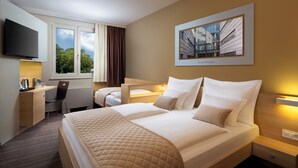 Une chambre d’hôtel avec un lit, un bureau, une chaise, une télévision et une fenêtre avec des rideaux.