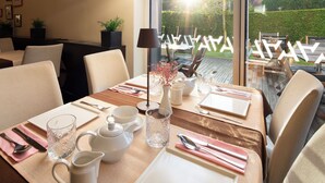 Une table à manger dressée avec de l’argenterie blanche, des couverts et des verres, donnant sur un jardin par la fenêtre.
