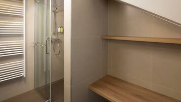 A modern bathroom with a glass shower enclosure, a white towel rack, and a wooden shelf.