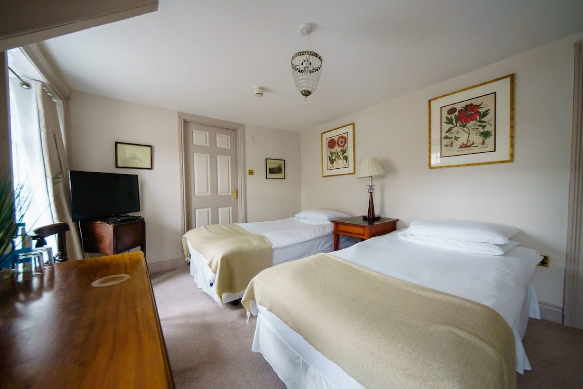 A hotel room with two beds, a television, a desk, and a chandelier.