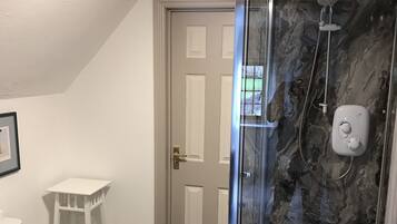 A bathroom with a glass-enclosed shower, a toilet, a small white vanity, and a door leading to another room.