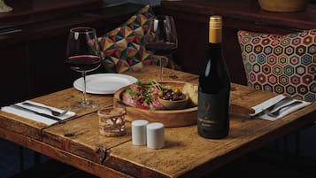 A wooden dining table set with a bottle of wine, glasses, a bowl of salad, and a plate.