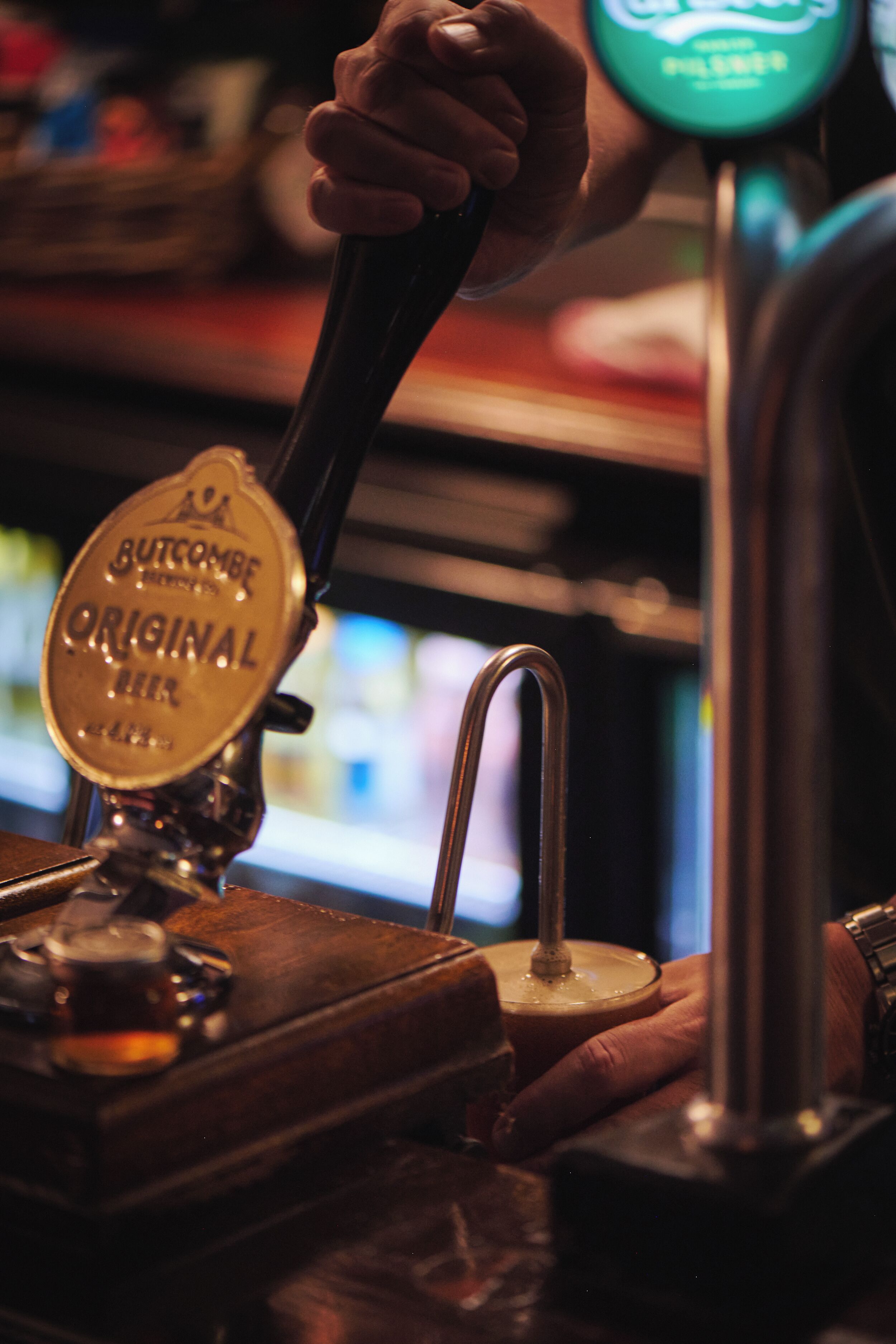Een hand bedient een biertapp met de tekst 'Butcombe Original Beer'.