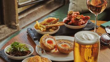 A wooden table with a variety of dishes, a glass of beer, and a window view.