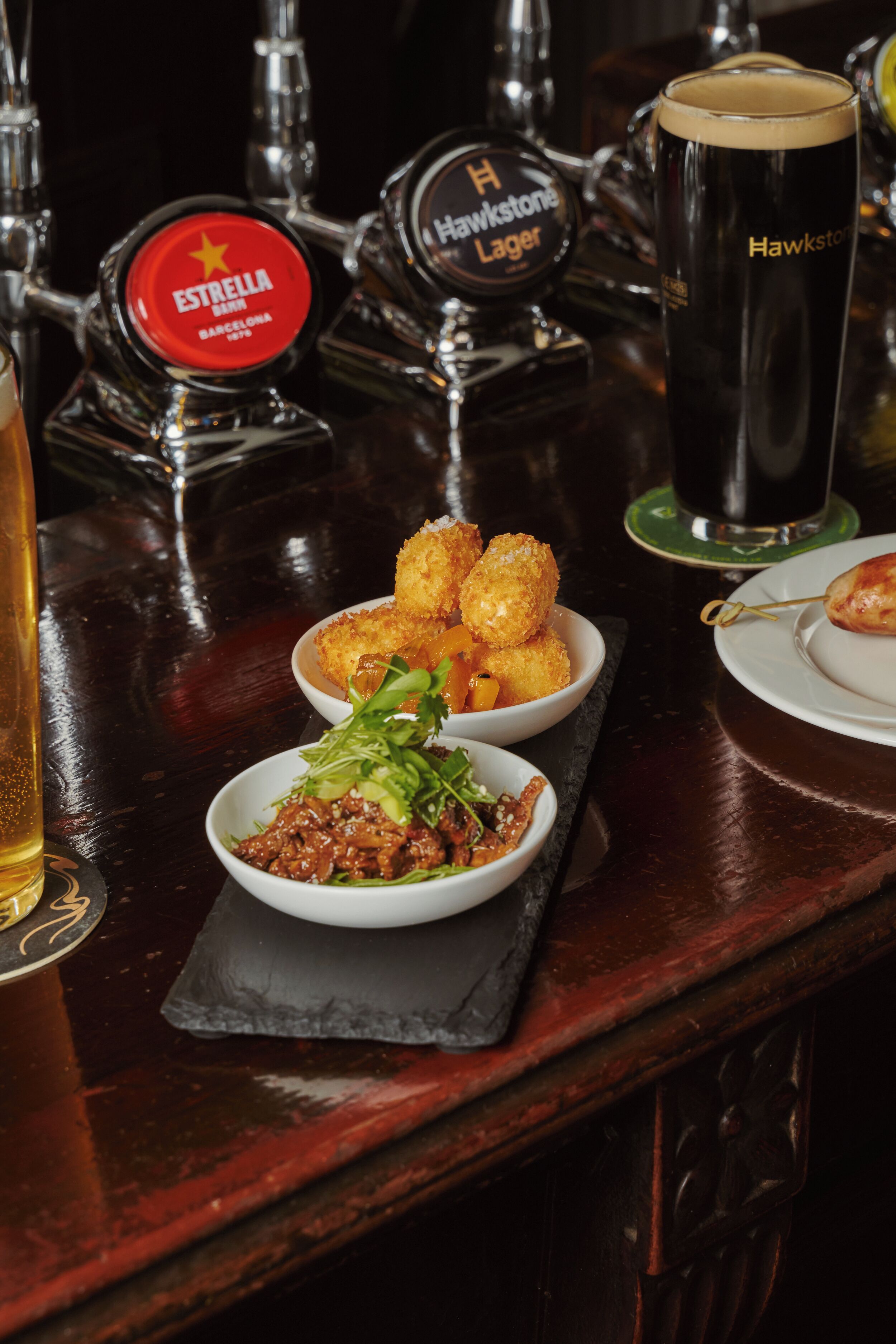 A bar with beer taps, a glass of beer, and food items on the counter.