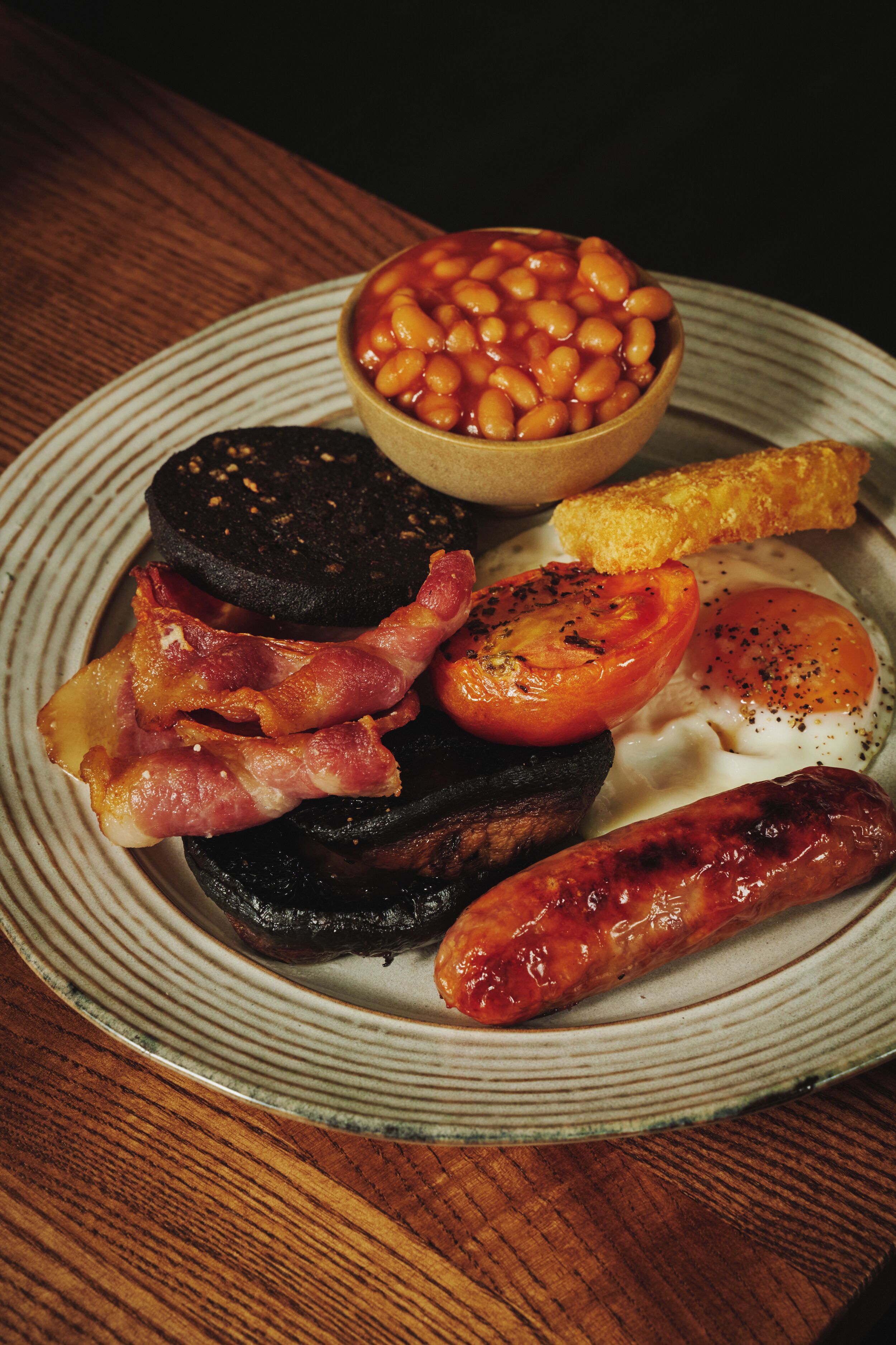 A plate of food with beans, bacon, tomatoes, eggs, and sausages.