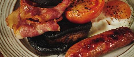 Un plato de comida con frijoles, tocino, tomates, huevos y salchichas.