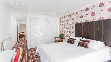 A bedroom with a large bed, a chair, a wardrobe, and a patterned wall.