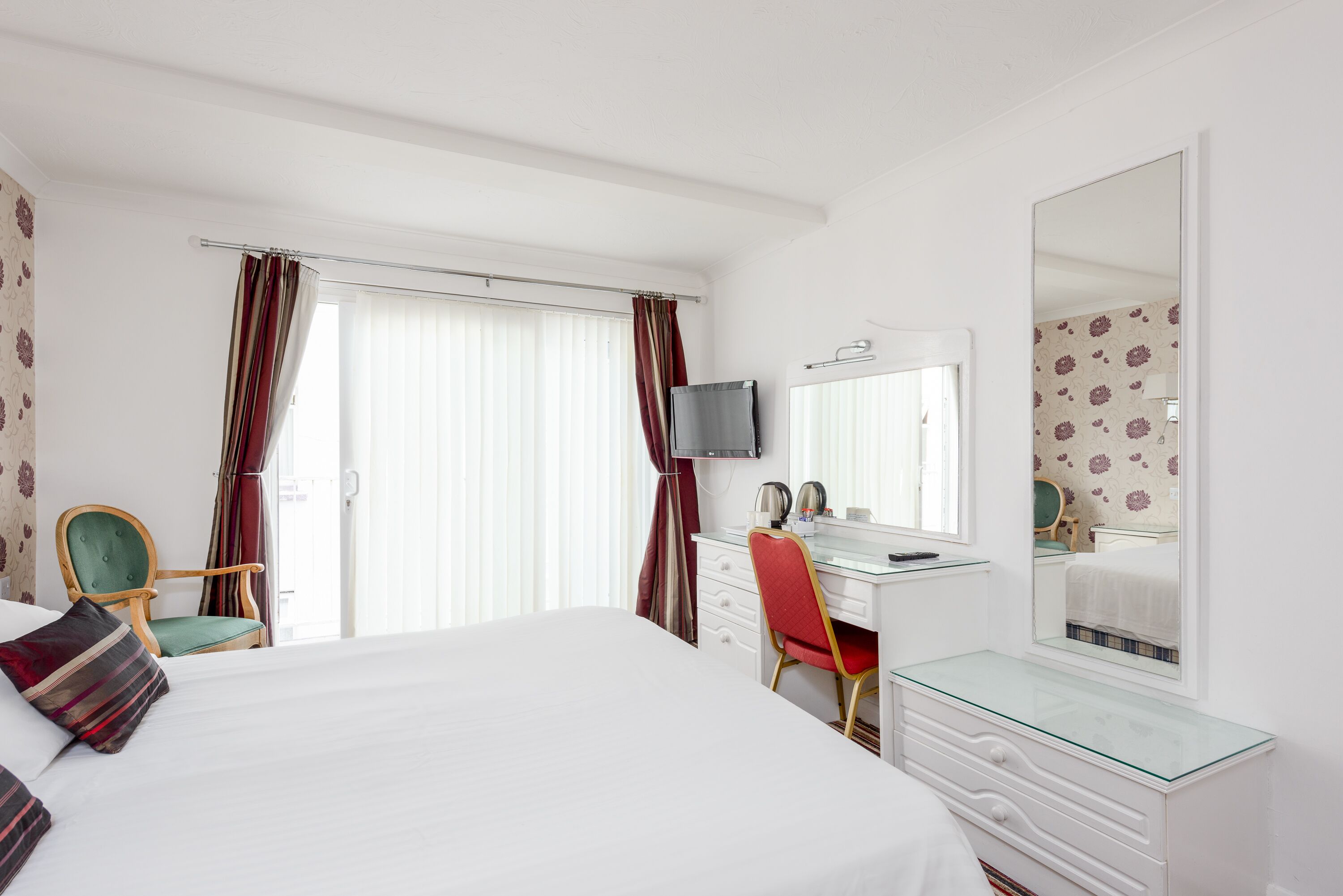 Une chambre d’hôtel comprenant un lit, un bureau, une chaise, une commode, un miroir et un téléviseur.