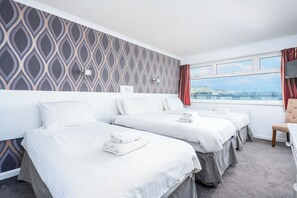 A hotel room with two beds, a chair, a window with a view, and a patterned wall.