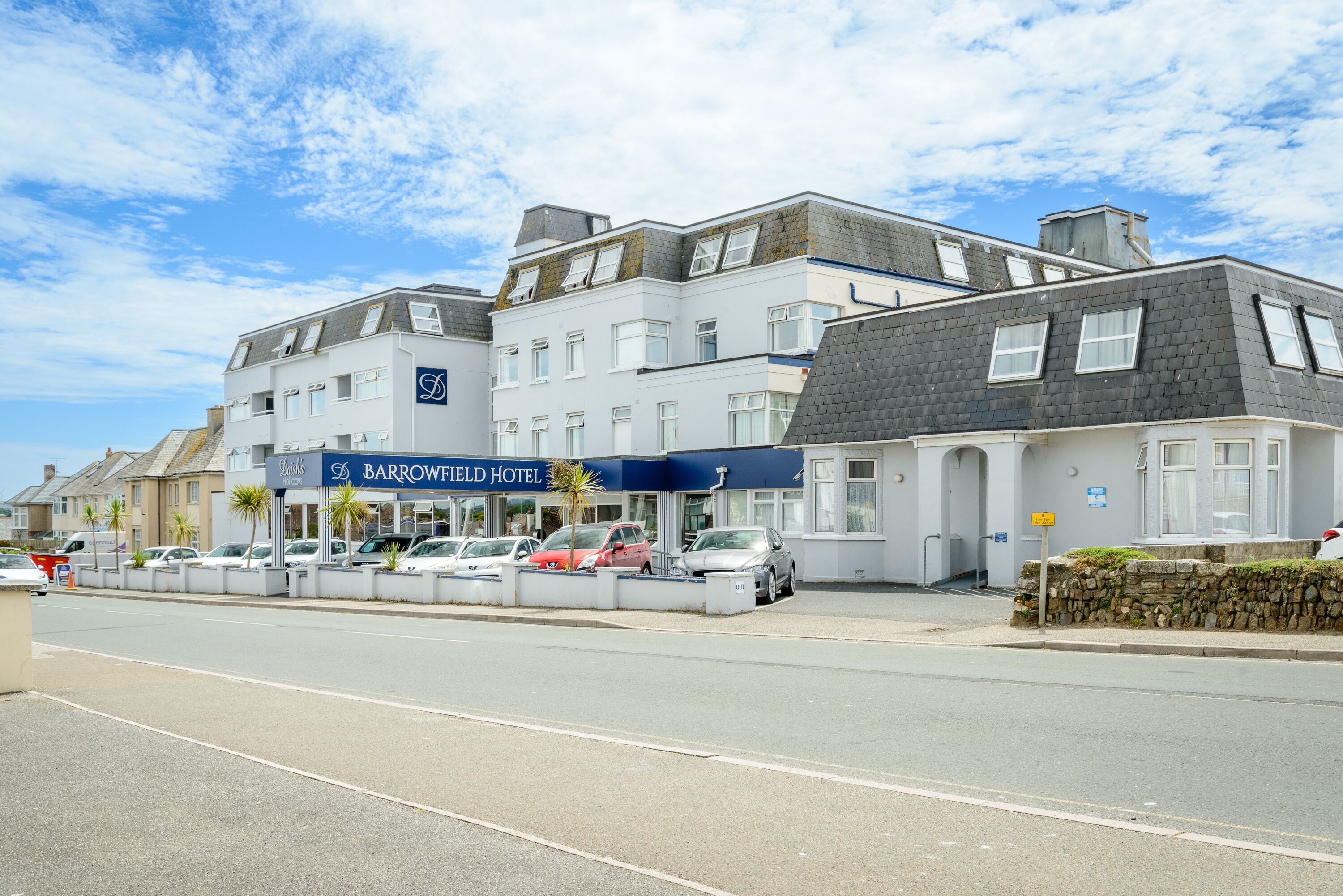 Ein mehrstöckiges Hotel mit auffälligem, blauem Schild, einem Parkplatz mit mehreren Autos und einem klaren Himmel.