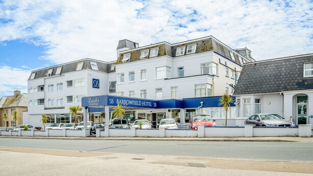 A multi-story hotel with a blue and white facade, several windows, and a parking area in front.