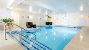 An indoor swimming pool with clear blue water, a metal ladder, and a palm plant. - Barrowfield Hotel (Newquay)