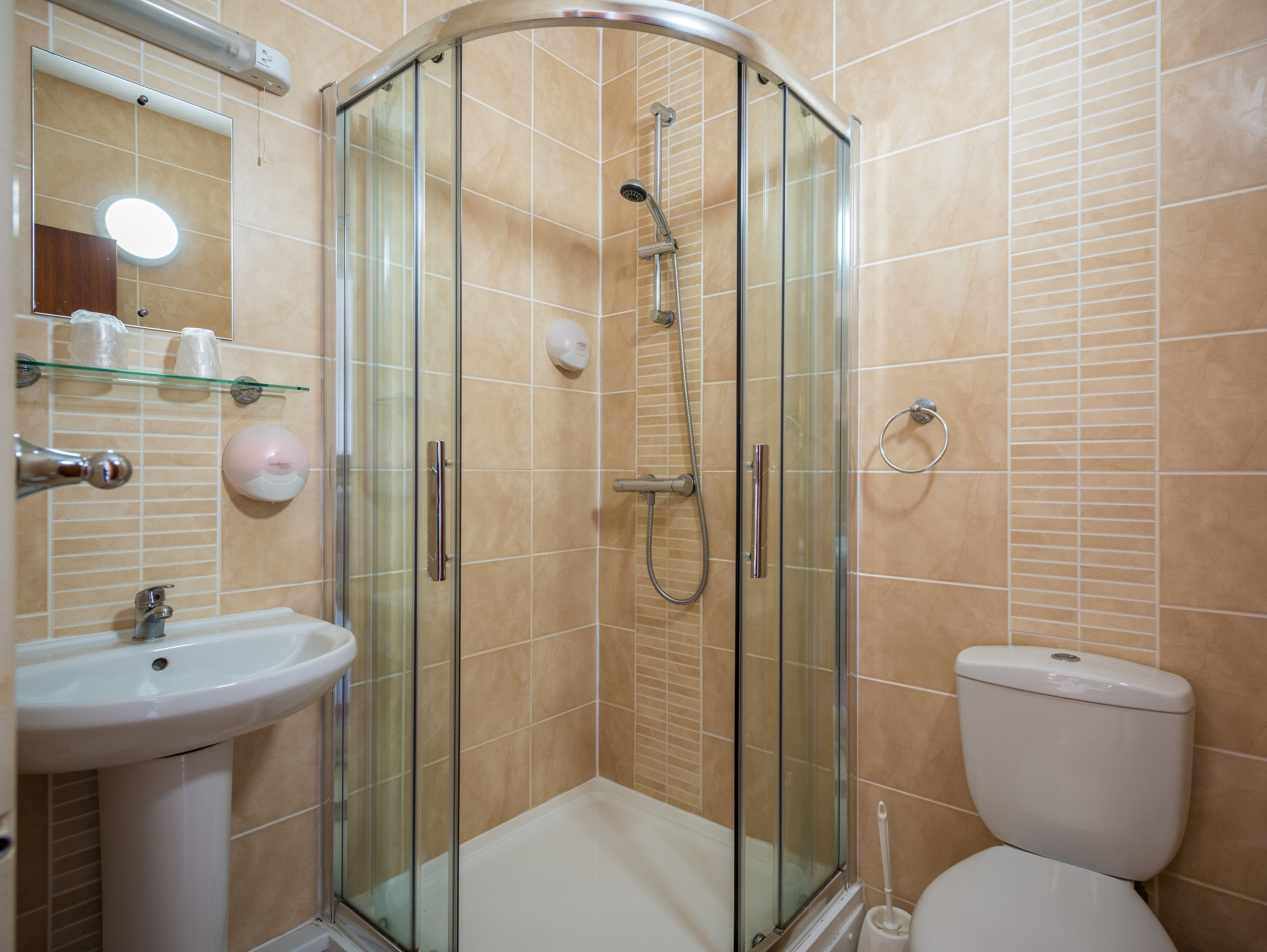 Un baño con ducha envuelta en vidrio, lavamanos e inodoro.