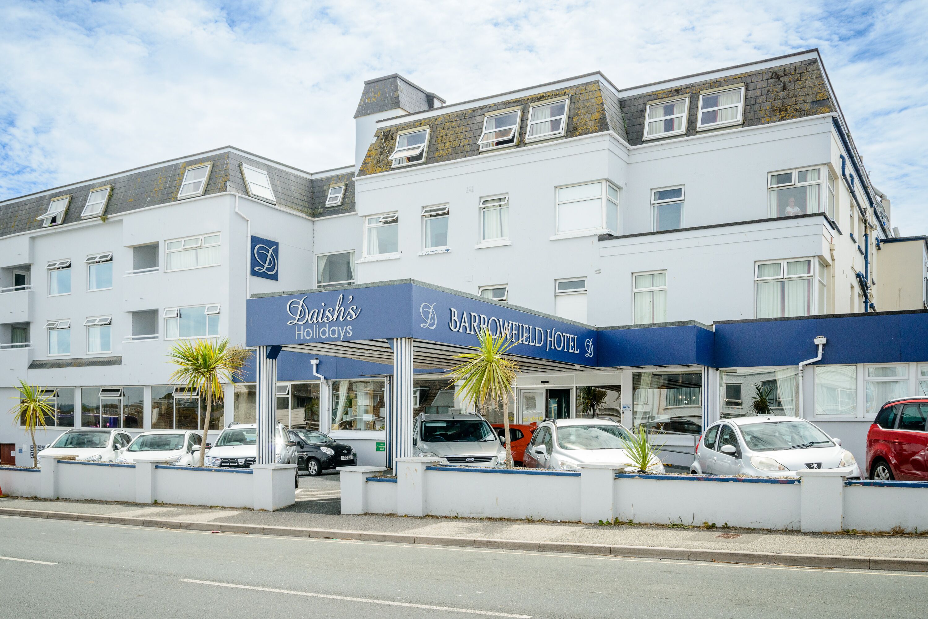 A multi-story hotel with a prominent blue and white facade, a covered entrance, and several parked cars.