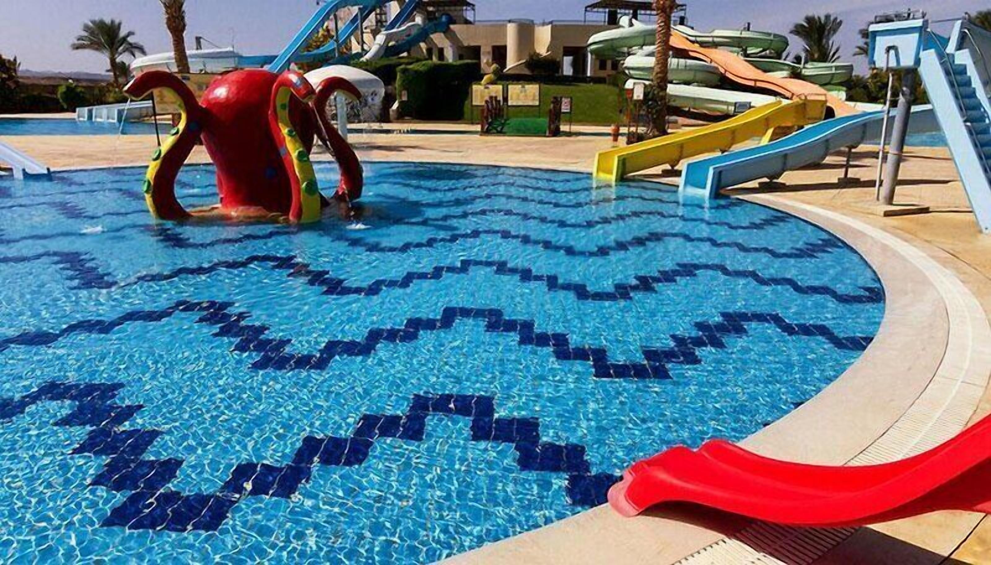Une piscine avec un motif en chevrons, une sculpture d’un poulpe rouge et un toboggan rouge.