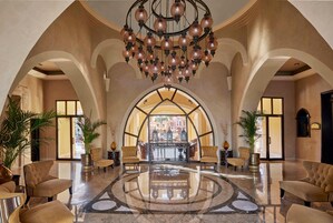 A spacious lobby with a high ceiling, a central chandelier, and a view through an arched doorway.
