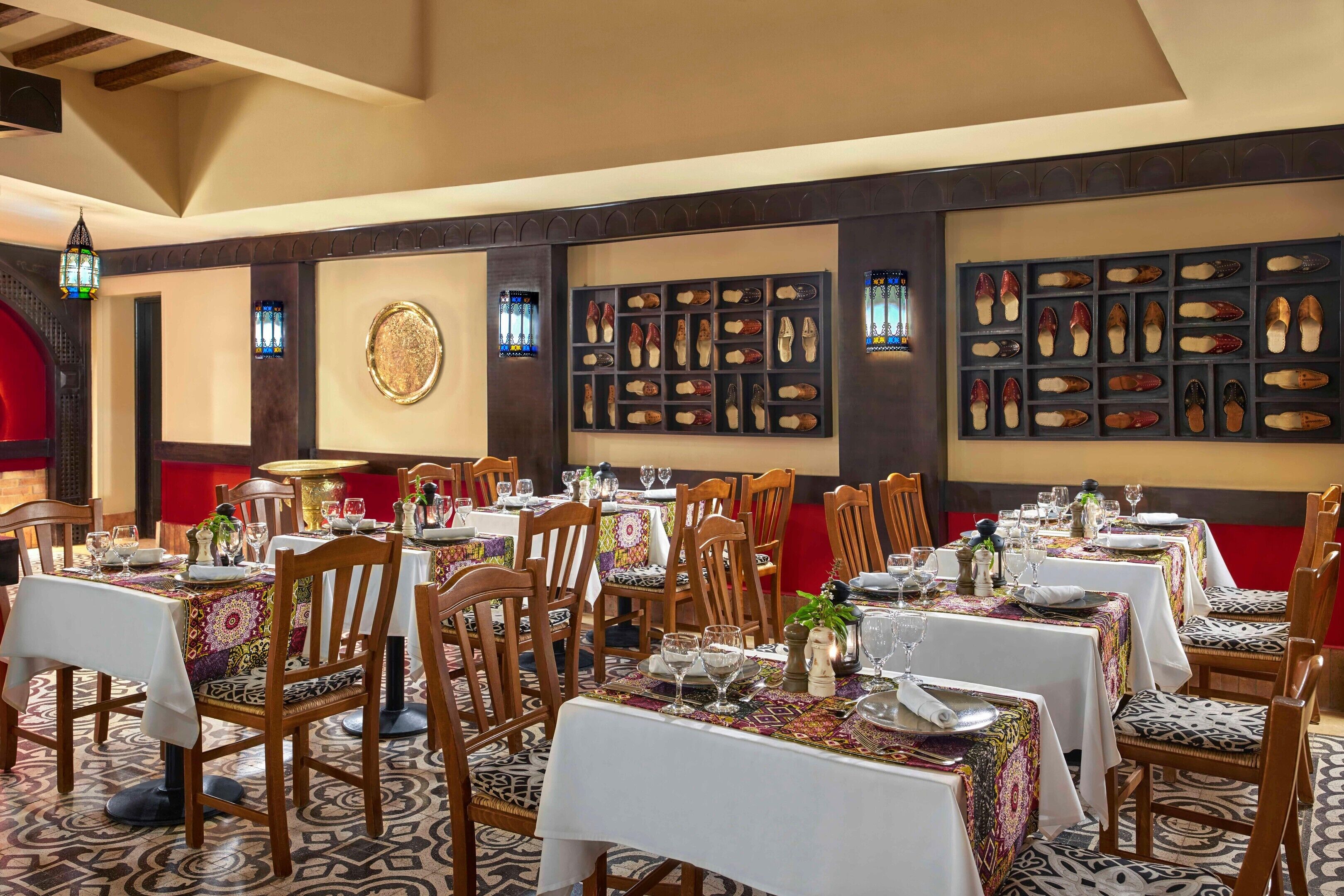 A dining area with tables set for service, wooden chairs, and a wall display of shoes.