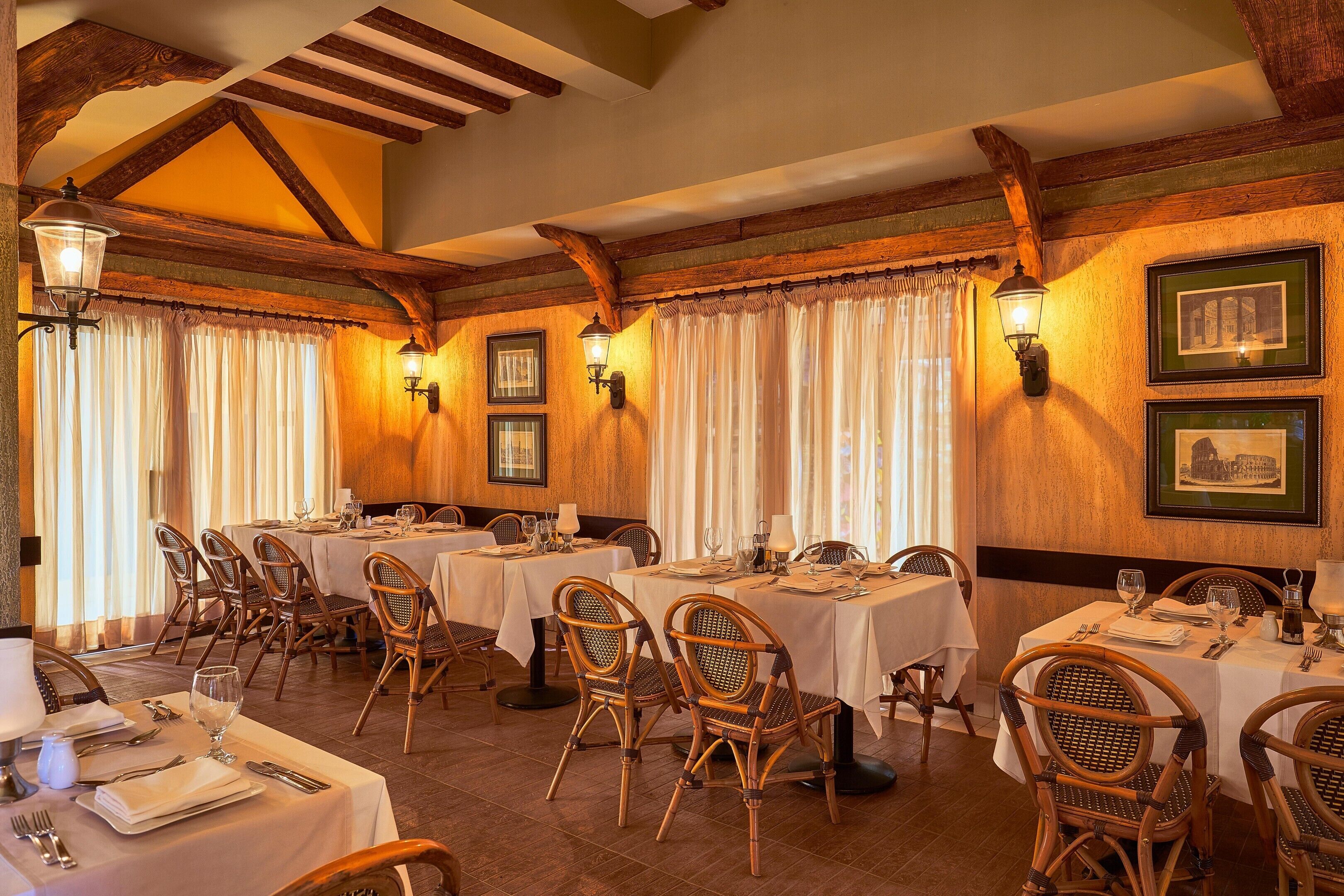 A dining area with tables set for four, wooden chairs, and wall-mounted lamps.