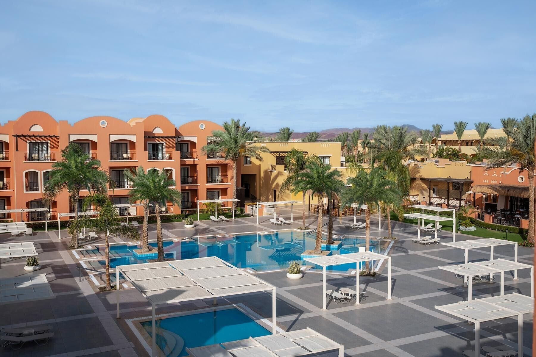 Un espace piscine d’hôtel comprenant plusieurs piscines, des chaises longues et des palmiers.