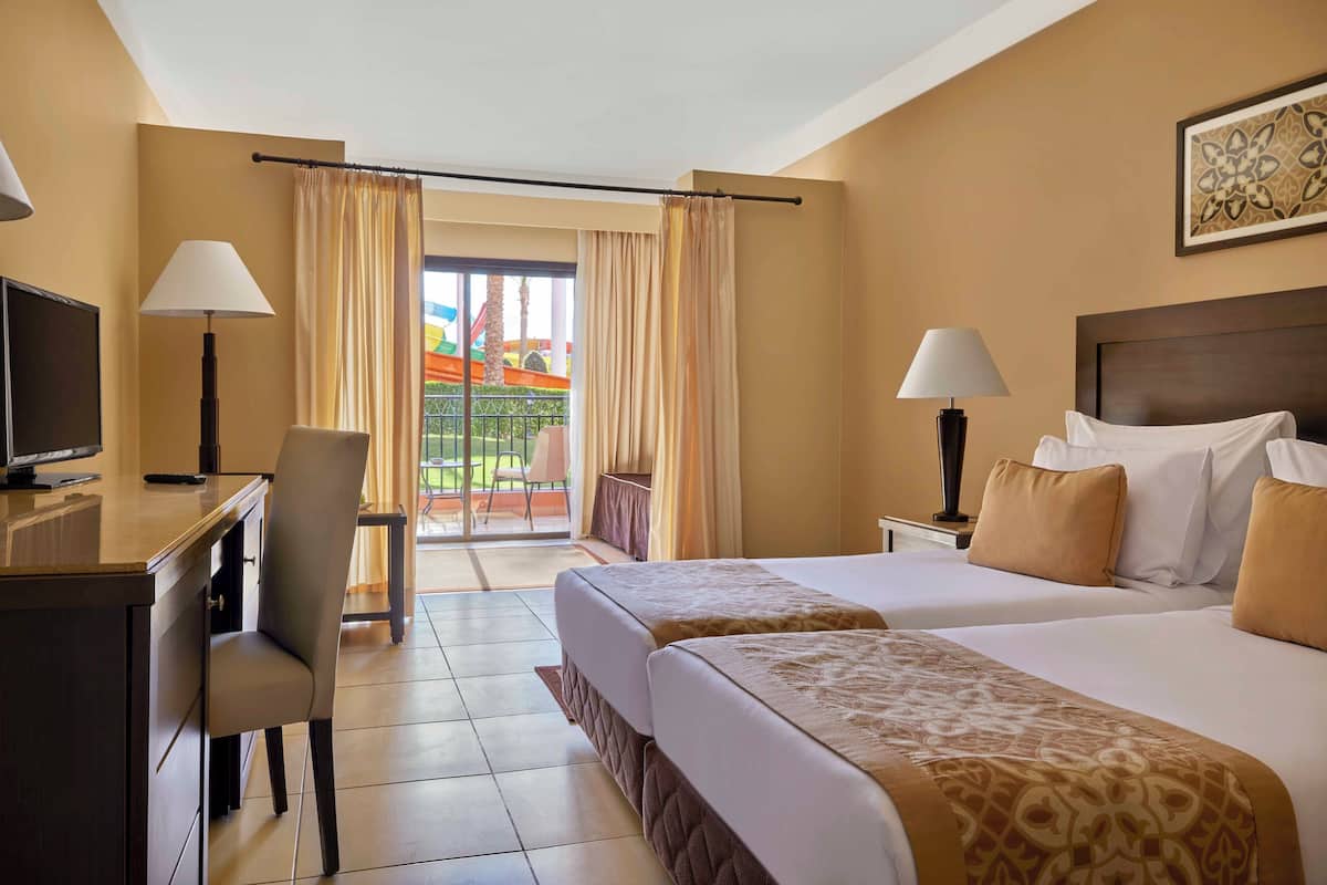 Quarto de hotel com duas camas, uma escrivaninha, uma cadeira e uma televisão.