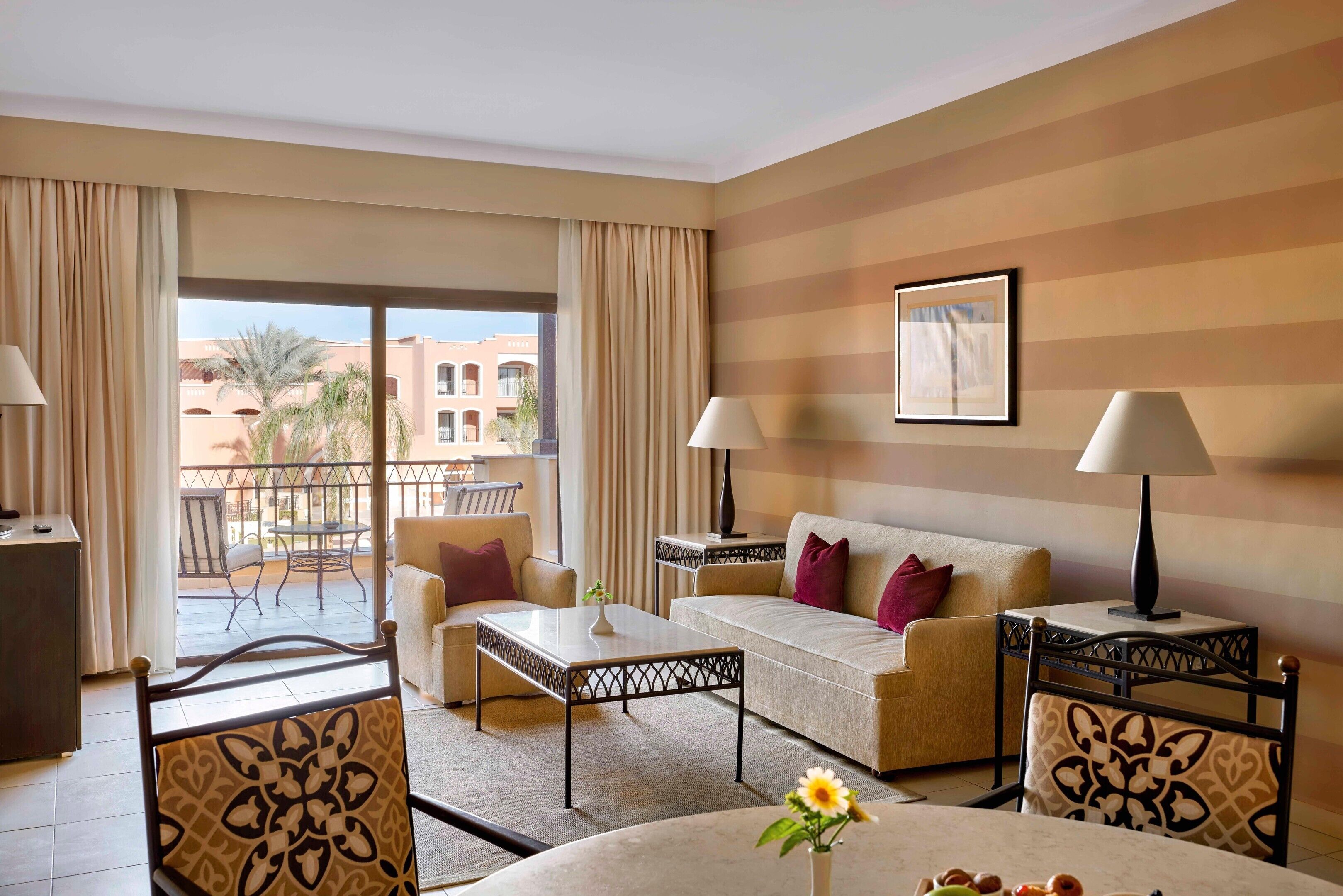 A hotel room with a balcony, a sofa, a coffee table, and a dining table.