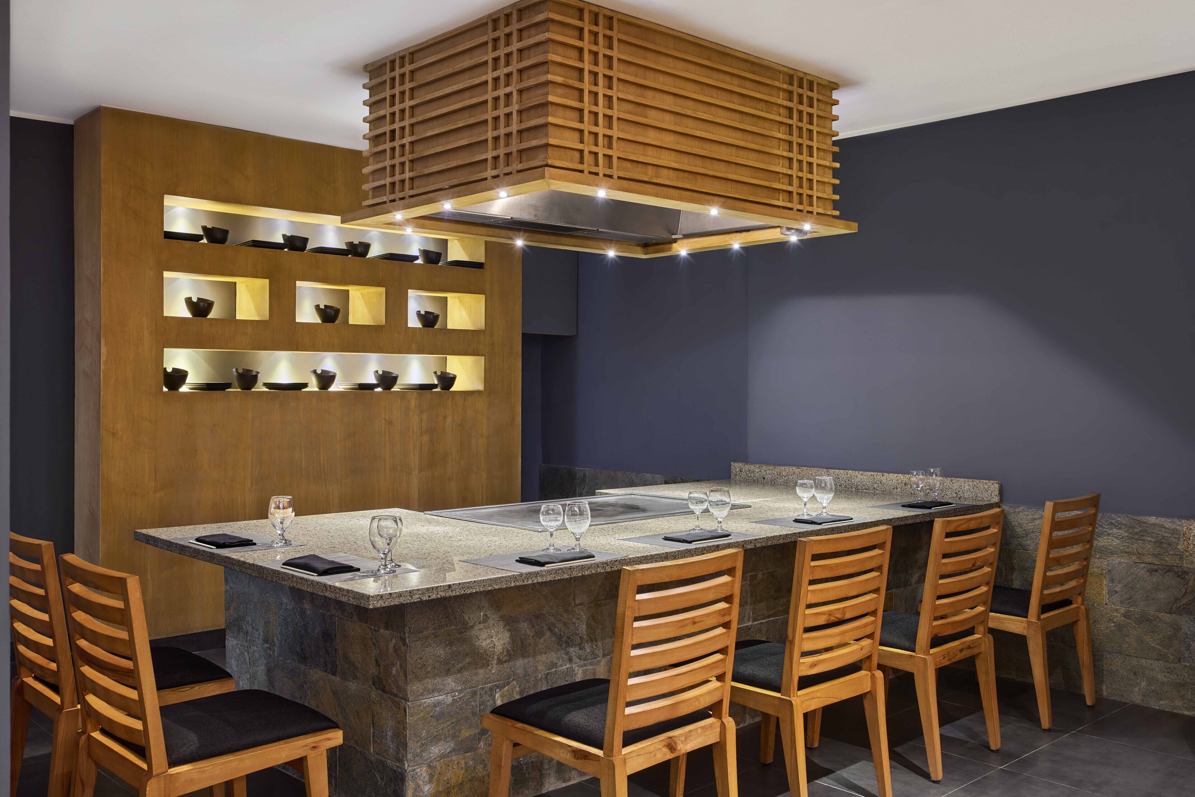 A modern dining area with a rectangular table, six wooden chairs, and a built-in shelf with multiple bowls.