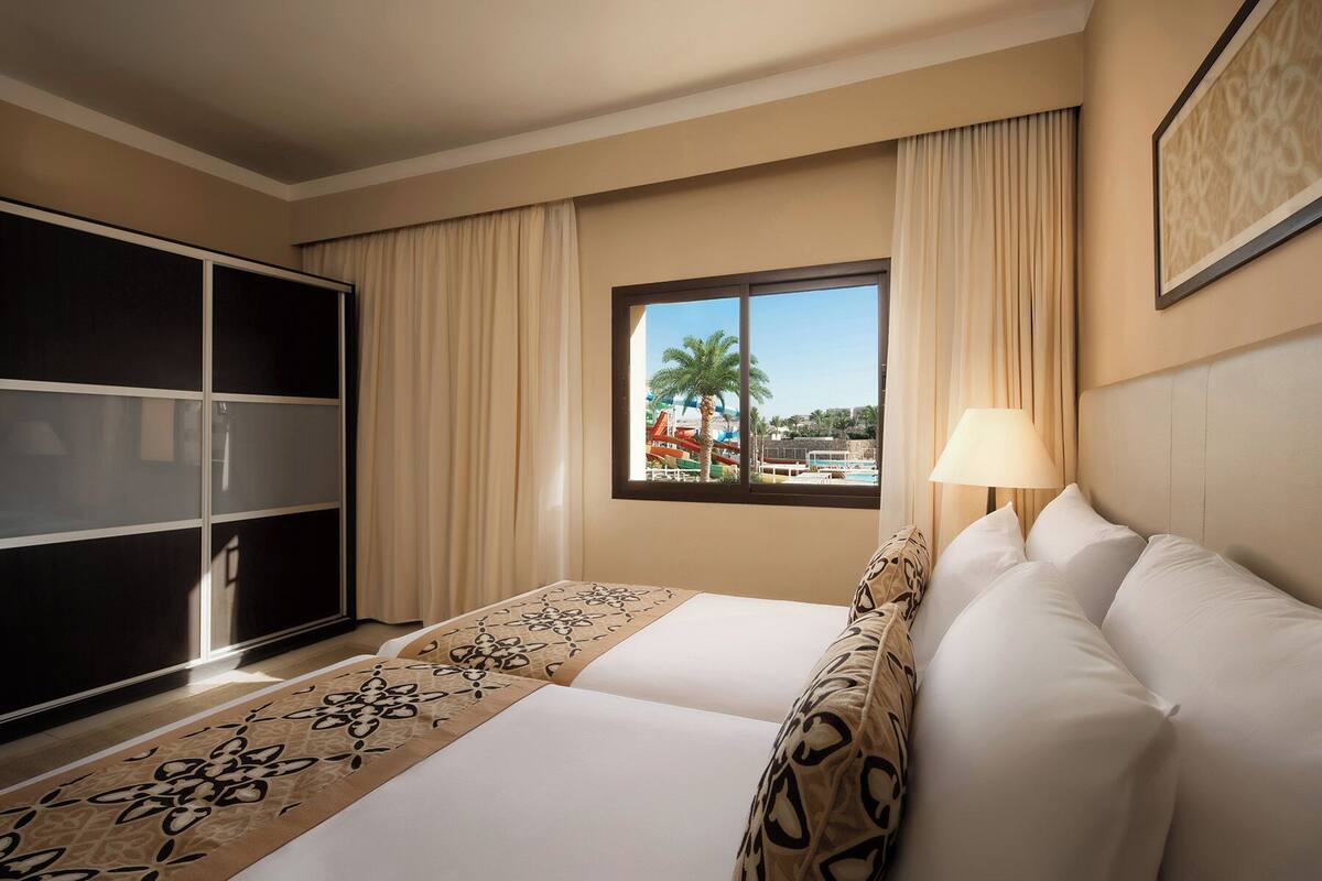 Quarto de hotel com uma cama grande, uma escrivaninha, um guarda-roupa e uma janela com vista para um parque aquático.