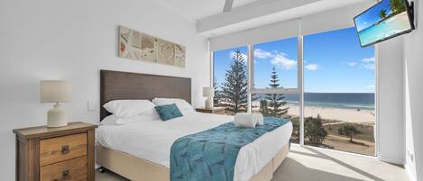 A bedroom with a bed, bedside table, lamp, artwork, ceiling fan, and a TV.