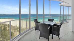 A balcony with a table and chairs, overlooking a beach and ocean. - Reflection Tower Two (Coolangatta)